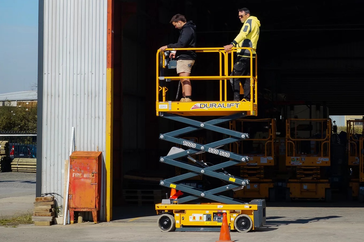 Two people on a raised Duralift scissor lift outside a warehouse.